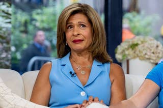 Person wearing a sleeveless blue top sitting on a couch during an interview, looking thoughtful