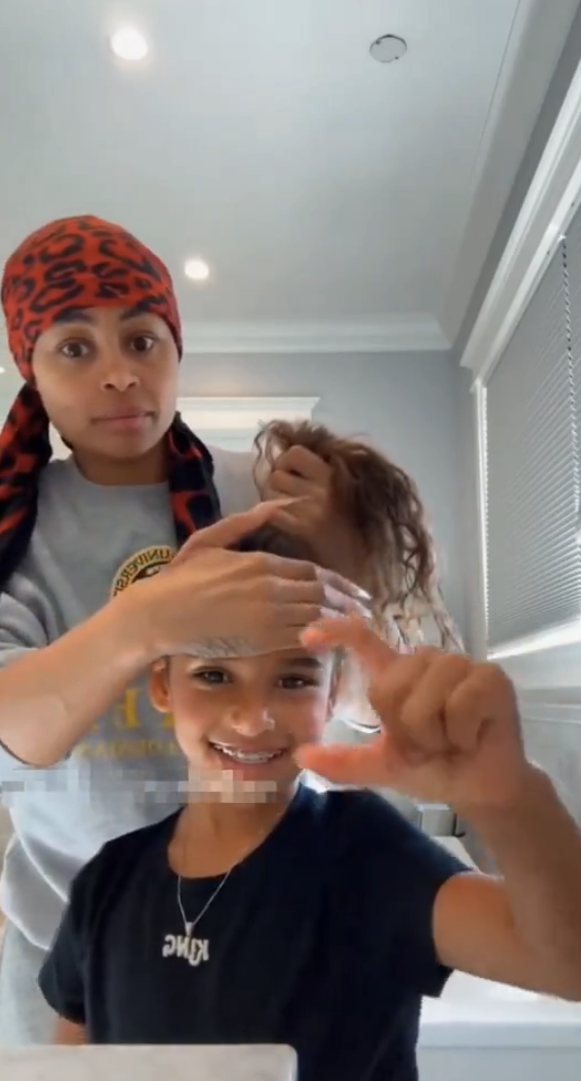 Blac Chyna stands behind a smiling child while fixing the Dream's hair