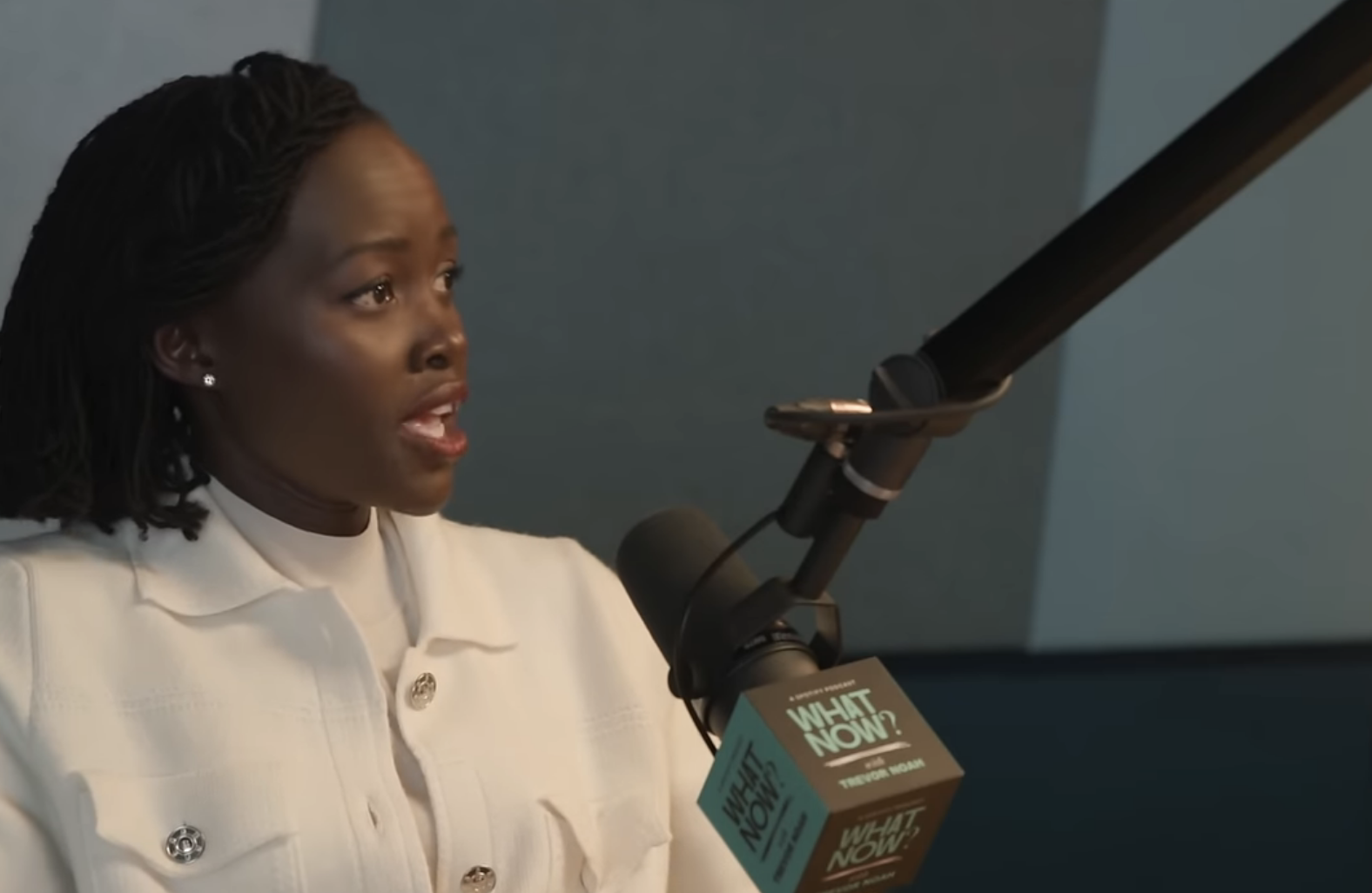 Lupita Nyong'o speaks into a microphone on the "What Now? with Trevor Noah" podcast